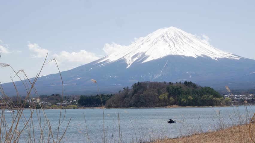 landscape cinematic scene of Mount Fuji famous volcano mountain with fountain grass field and lake kawaguchi perfectly reflected on the still waters of the Lake with windy and clear sky in spring