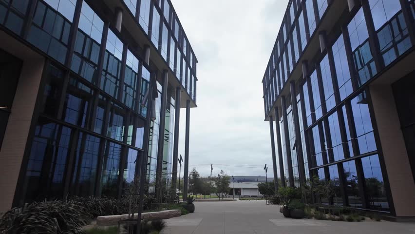 Slow forward movement through an empty courtyard between two contemporary glass buildings, which are part of a medical laboratory campus in South San Francisco, California on a cloudy day