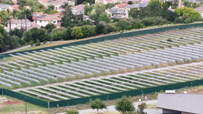 Aerial perspective of a large solar panel farm producing renewable energy, located adjacent to a suburban residential neighborhood and the Evergreen Valley College in San Jose, California