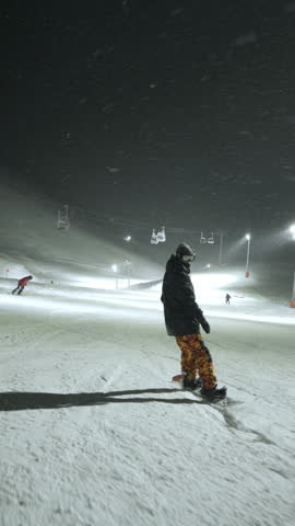 Snowboarder riding on a mountain slope during a heavy night snowfall.