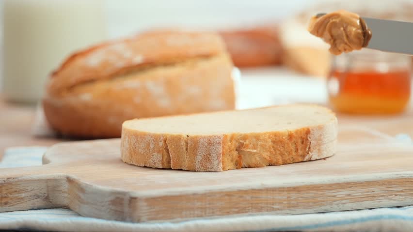 Peanut butter spread on fresh bread slice, homemade breakfast preparation, copy space