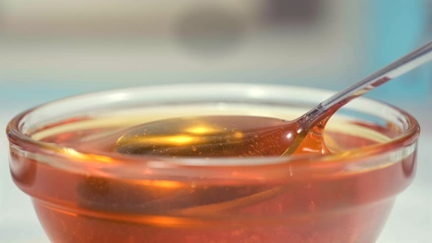 Honey dripping from spoon into glass bowl macro food texture dessert syrup copy space