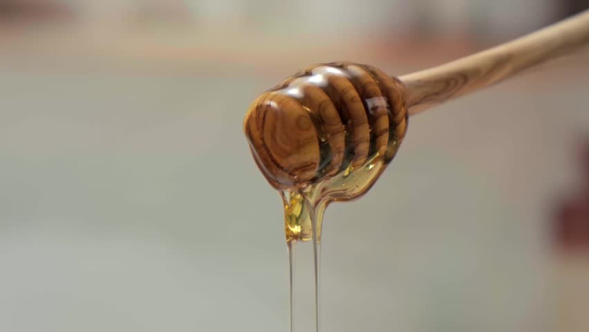 Honey dripping from wooden dipper, macro food texture dessert syrup copy space