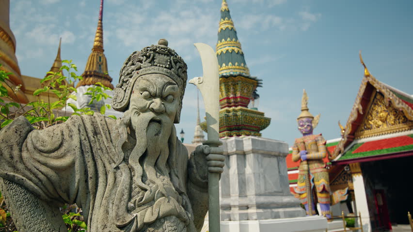 Ancient stone guardian holding sword at Wat Phra Kaew in Bangkok, iconic Thai temple complex and cultural landmark.