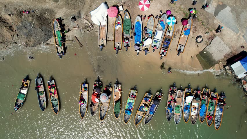 Aerial view of traditional wooden motorboats lined up along the muddy riverbank with people and colorful umbrellas in Wewak, East Sepik Province, Papua New Guinea.