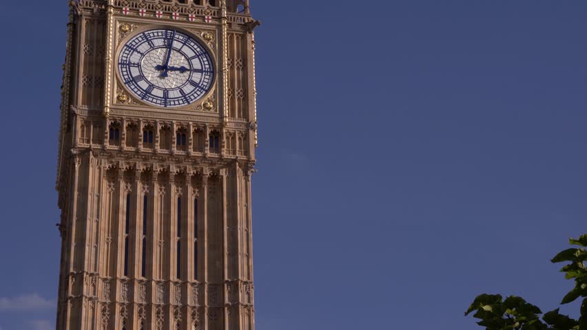 Detailed close-up of the Big Ben clock face under a clear blue sky

A stunning architectural close-up of the iconic clock face on the Elizabeth Tower, famously known as Big Ben, at the Palace of Westminster in London. The footage highlights the intricate golden details, the classic blue clock hands, and the masterful Gothic Revival stonework. Captured on a bright morning with a crisp blue sky, this shot emphasizes the timeless elegance and historical significance of one of the world