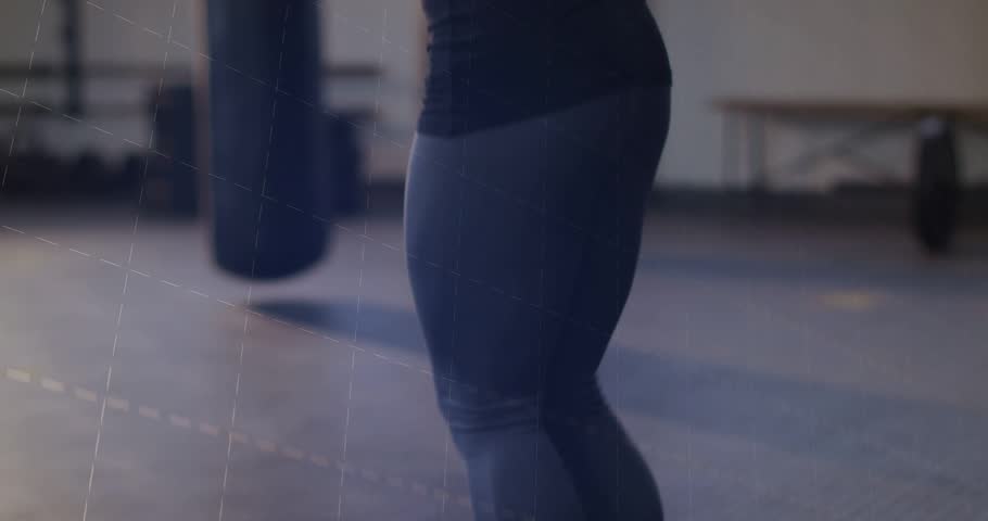 Mid-adult woman starting closeup jumping rope training at gym by heavy bag in tank leggings data. Female, cardio, studio, fitness, rhythm, motion, overlay