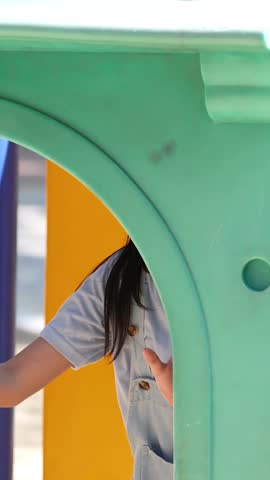 A happy young Asian girl smiles while playing on colorful outdoor playground equipment in Bangkok