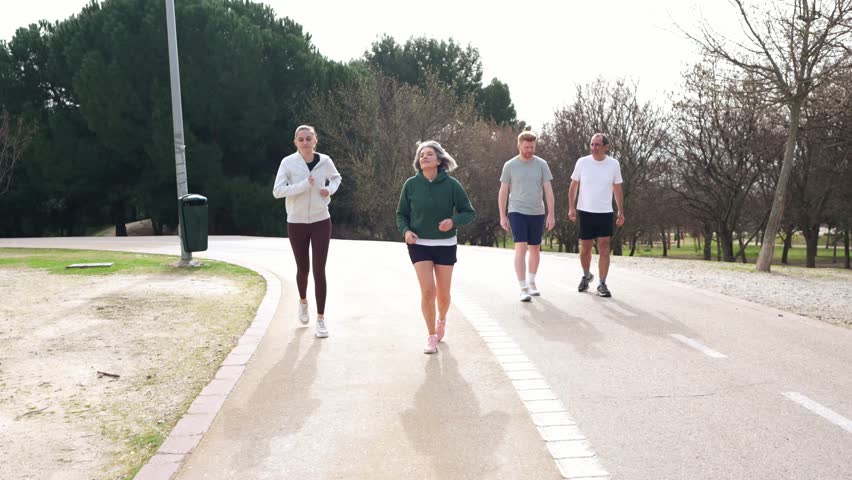 Diverse group of friends, including seniors, jogging together on a path in a public park. Healthy lifestyle and outdoor exercise concept