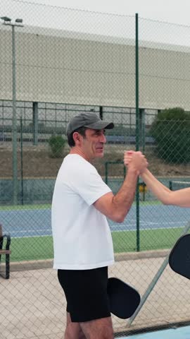 Smiling mature man in sportswear hitting the ball with a paddle on a blue pickleball court. Active lifestyle and friendly competition