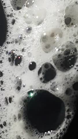 The texture of soap foam bubbles on a dark surface flowing down slowly from top to buttom.