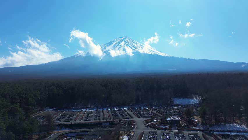Drone aerial landscape of Mount Fuji snowy peak covered in foggy clouds along the skyline with rural forest trees and a national park in the valley near Kawaguchiko Yamanashi Japan Asia nature travel