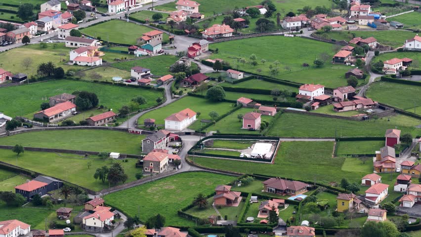Aerial view of a rural village featuring red-roofed houses and lush green fields in Asturias, Spain.