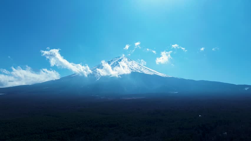 Drone aerial landscape of Mount Fuji landmark covered in clouds on a snowy peak summit surrounded by woodland forest trees in the valley near town of Kawaguchiko in Japan lakes district Asia nature