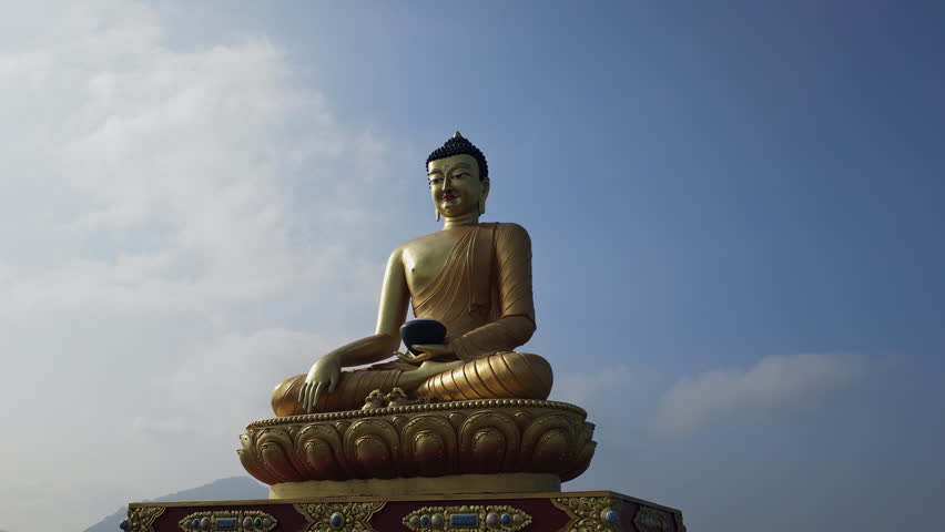 Golden Buddha statue seated in meditation posture against clear blue sky in a serene outdoor setting.