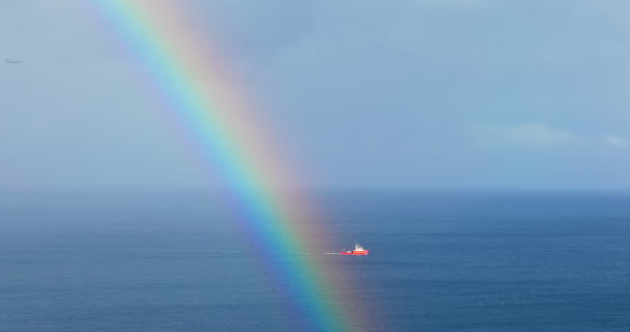 Vibrant Rainbow Arch Against a Deep Blue Sky and White Clouds over Sea horizon and sailing boat