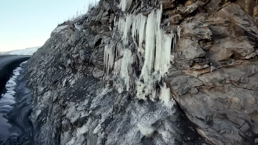 Frozen icicles cling to a textured rock face. A wintry landscape showcases the beauty of natural ice formations.