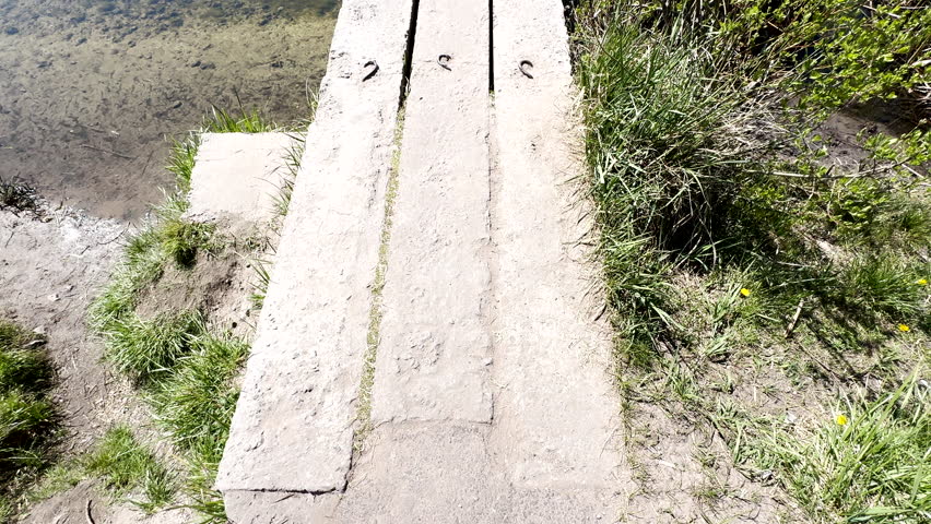 POV of a man in red pants balancing on a narrow concrete edge by the river. Carefully stepping down towards clear water, concept of risk and focus.