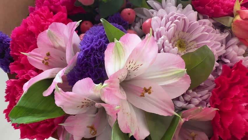 Smooth camera movement over mixed flower bouquet revealing hot pink carnations lavender chrysanthemum pink alstroemeria purple statice and coral hypericum berries 4K footage.