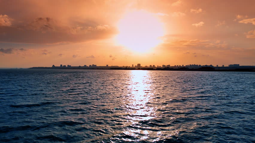 Sunset over the city skyline and water. The sun is setting over the water, casting light on the city skyline in the distance during evening hours.
