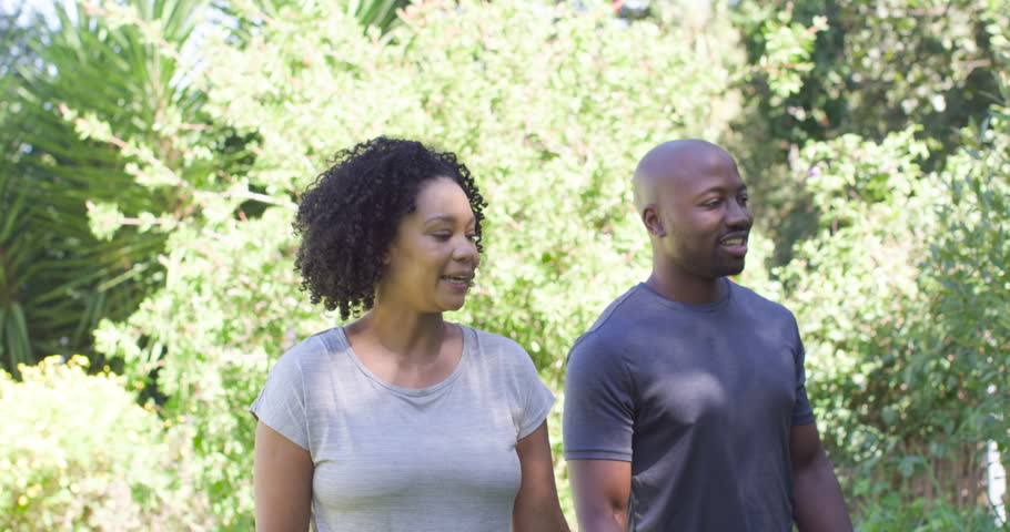 African American couple standing by yard plants, man seeing offscreen view, pointing, woman leaning. Pair, garden, outdoor, daylight, greenery, palms, blossoms