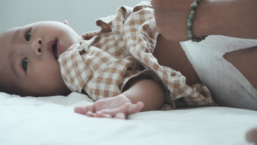 A seven-month-old boy is lying in bed, rolling over and crawling on the mattress in his bedroom at home.

