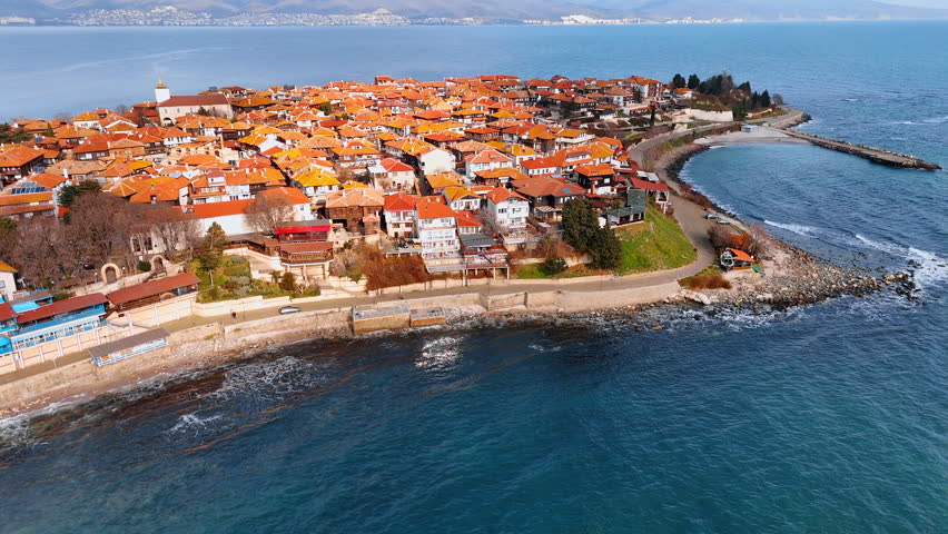 Coastal town view with houses and water. Aerial view of a coastal town with many houses and a beach. Waves crash against the shore in a clear blue sea.