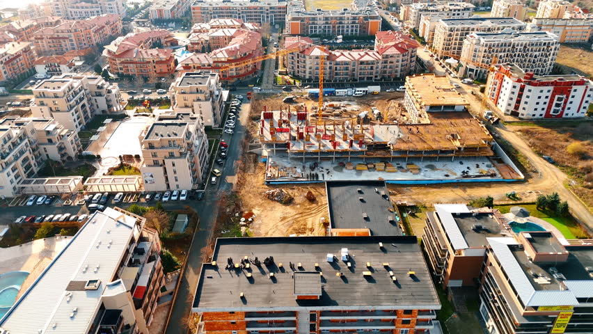 City area construction update. Workers are building new structures in an urban area with several buildings and a clear blue sky during daylight.