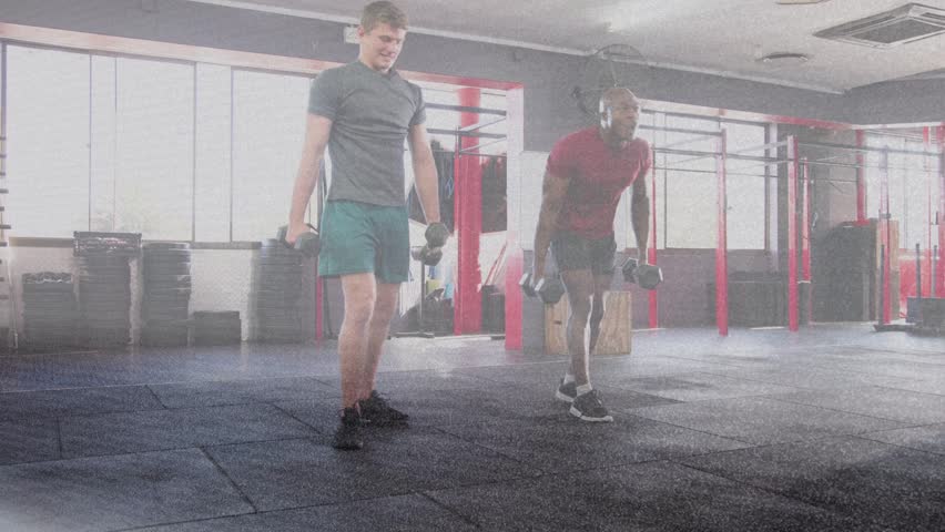 Two men starting side-by-side, doing in-sync dumbbell walking lunges across gym mat for strength. Exercisers, partners, training, fitness, synchronized, weights, studio