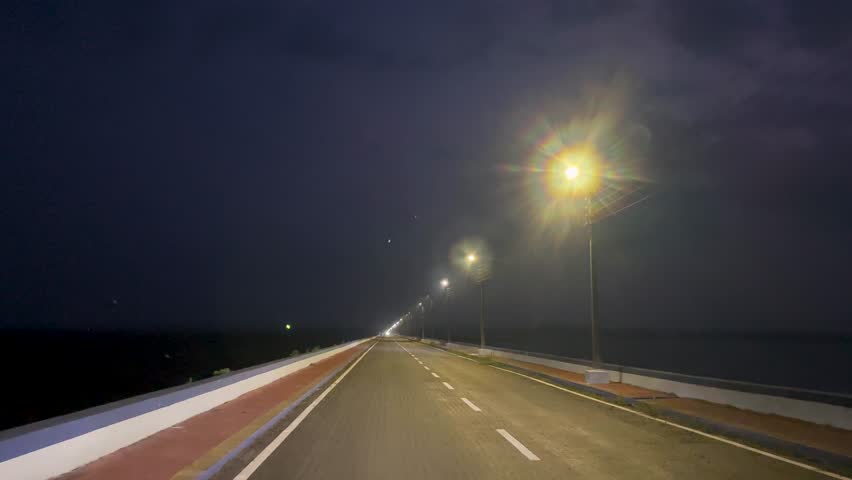 Driving on deserted bridge at night, streetlights, long road perspective, dark sky.