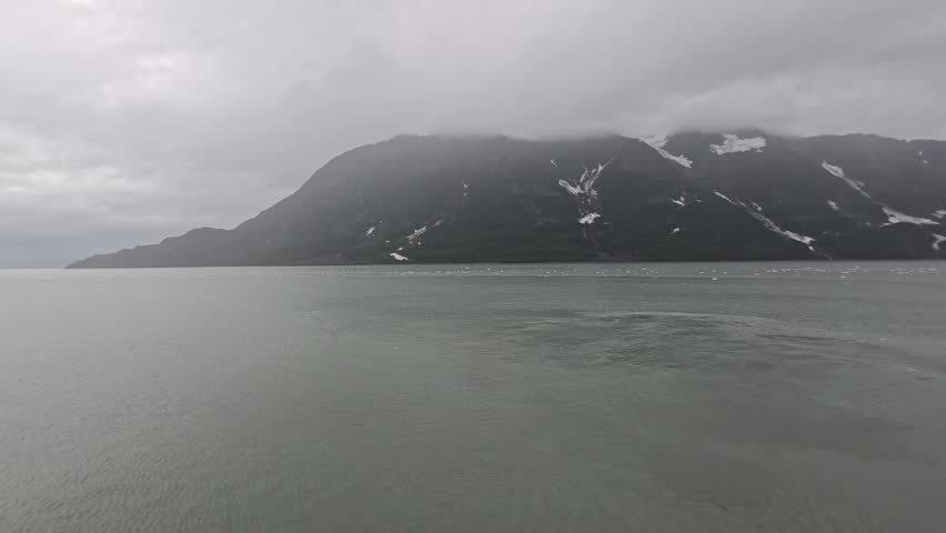 Alaska, USA - Hubbard Glacier meets Disenchantment Bay, forming a dramatic landscape where ice calves into the water below cloudy mountains. Misty conditions enhance the region. Overcast conditions fill the sky.