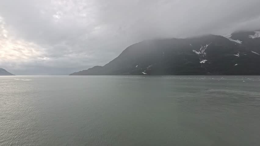 , USA - View of Hubbard Glacier landscape with mountain range partially covered in clouds reflecting in the ocean bay waters in Alaska.
