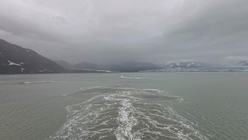 Alaska, USA - View of the Hubbard Glacier and its surrounding waters. A boat trail creates white water contrasting to the glacier and overcast sky.