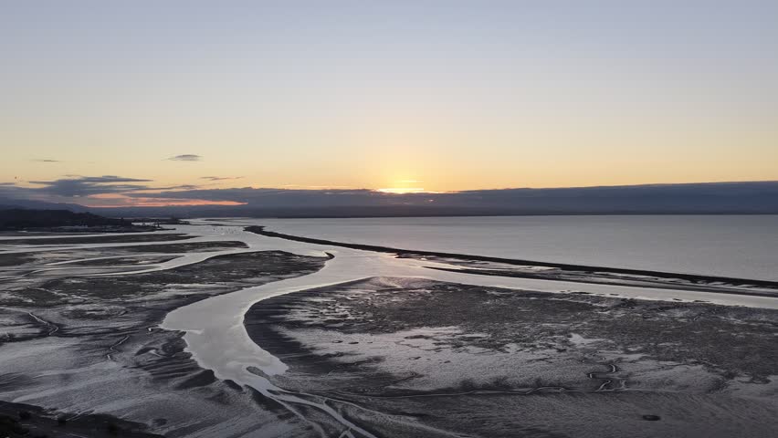 Winding river through tidal flats meeting sea at sunset in New Zealand