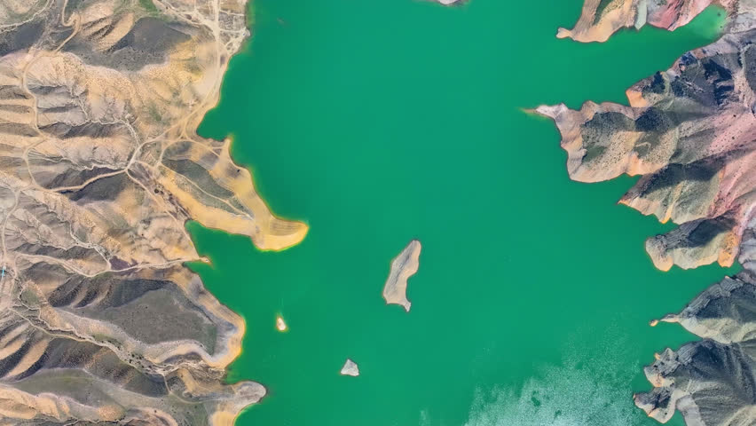 Aerial view of a vibrant green lake surrounded by rugged, arid mountains