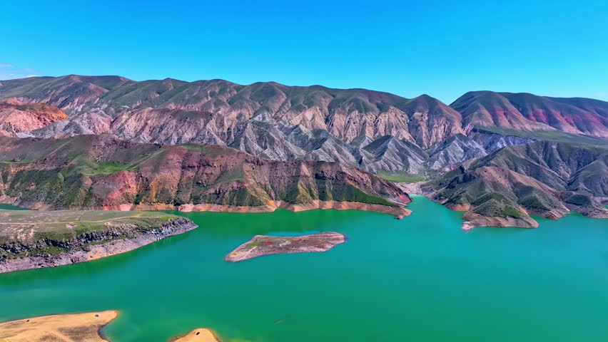 Drone shot captures vibrant river snaking between colorful mountain ridges