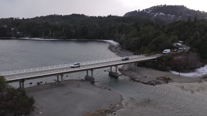 Traffic flows across a bridge spanning tranquil waters and lush forests in Río Negro Province, Argentina. Ideal for travel content or infrastructure features.