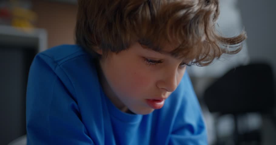 Focused young boy in a blue shirt drawing with a yellow pencil on paper, close-up view of childhood creativity, concentration, and learning at home