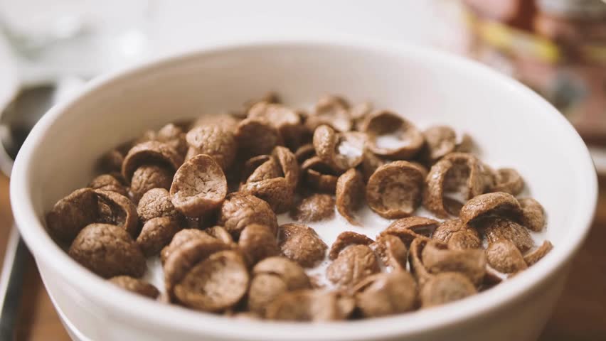 Chocolate flakes or chocolate crunch cereal for morning breakfast. milk falling in to the cocoa cereal. Milk Being Poured onto the Chocolate Cornflakes.
