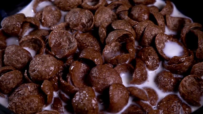 Milk Being Poured onto the Chocolate Cornflakes. pouring milk into a bowl with chocolate cereals. Chocolate flakes or chocolate crunch cereal for breakfast.