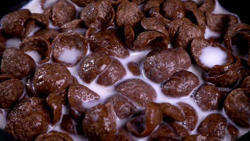 Milk Being Poured onto the Chocolate Cornflakes. pouring milk into a bowl with chocolate cereals. Chocolate flakes or chocolate crunch cereal for breakfast.