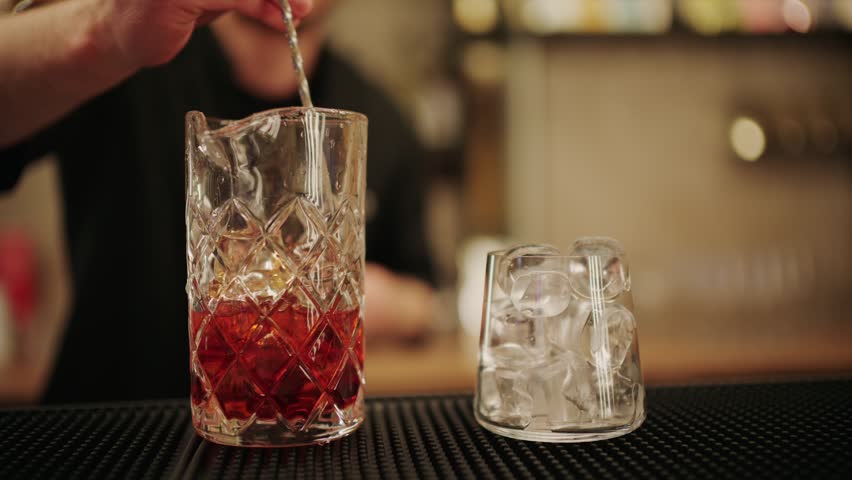 Bartender stirring cocktail with ice in mixing glass for refreshing drink.