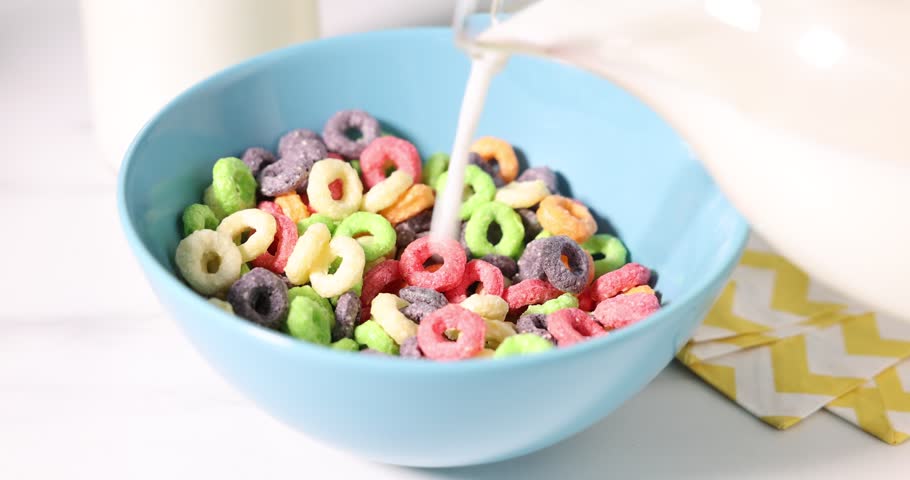 Pouring milk into bowl of delicious cereal on white wooden table, closeup