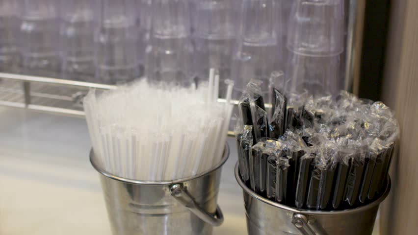 Close-up shot of a hand selecting wrapped plastic straws from a metal bucket in Bangkok