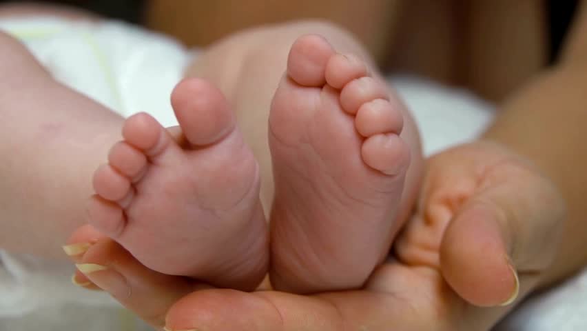 Mom holds the little feet of the newborn baby. Mother caresses the child