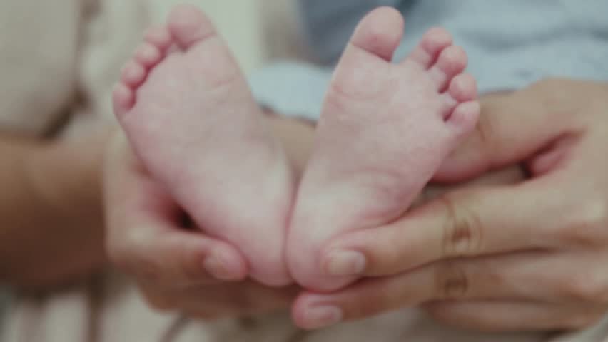 Mom holds the little feet of the newborn baby. Mother caresses the child
