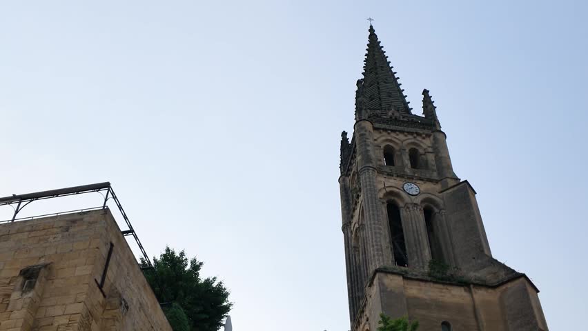 Low angle view of a historic stone church steeple against a clear blue sky