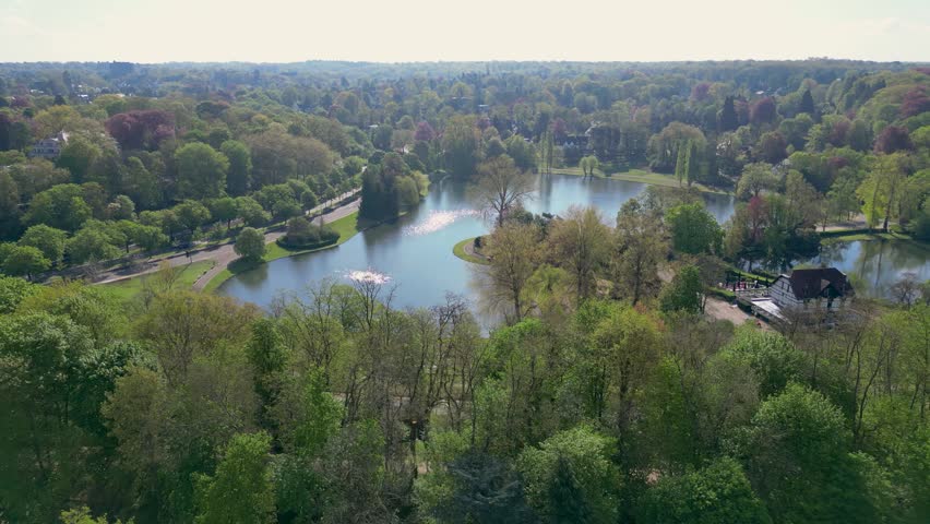 Aerial view of the scenic Woluwe Park featuring a calm lake surrounded by dense green trees and walking paths in Woluwe-Saint-Pierre, Bruxelles, Belgium.