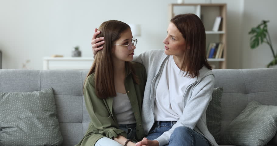 Mother and daughter talking sit on couch in living room at home, showing love, understanding and warm relationships between teen and parent. Family connection, interpersonal communication, bonding