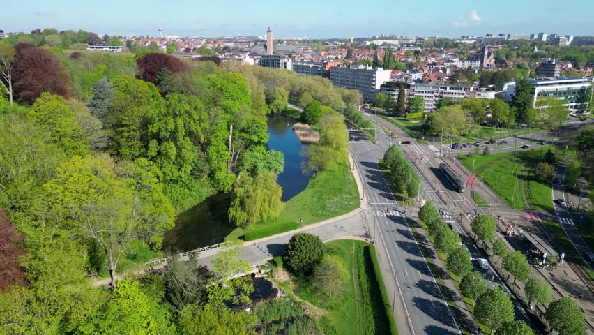Aerial view of a lush park with a pond and tram tracks alongside a road in Woluwe-Saint-Pierre, Bruxelles, Belgium.